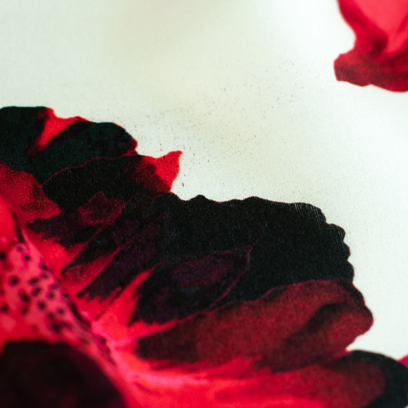 Italian Floral Silk satin designer deadstock fabric by the yard. Ready to create something gorgeous with our silk satin fabric of red and pink blooms highlighted by a bit of black for drama set against a white background. This thin woven silk from the Italian mills has a smooth satiny hand and just the right amount of flow! Image of fabric printing defect.