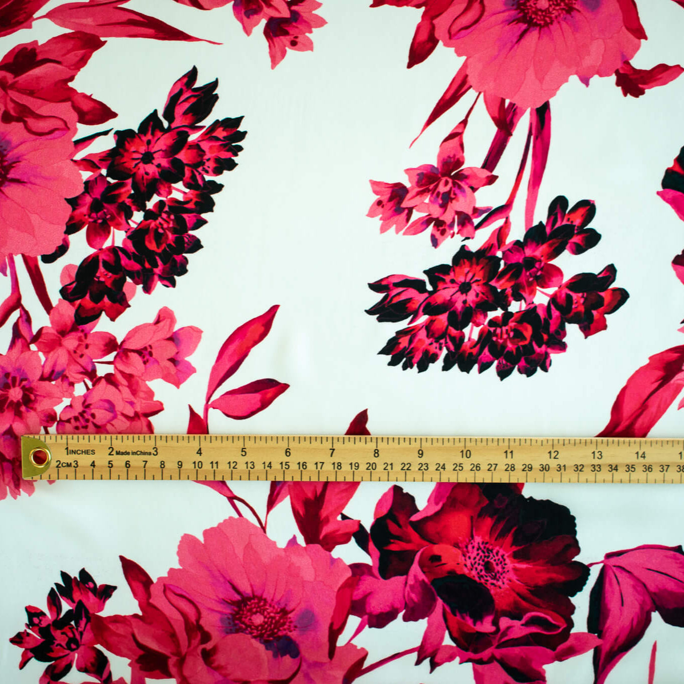 Italian Floral Silk satin designer deadstock fabric by the yard. Ready to create something gorgeous with our silk satin fabric of red and pink blooms highlighted by a bit of black for drama set against a white background. This thin woven silk from the Italian mills has a smooth satiny hand and just the right amount of flow! Image of fabric design scale with ruler.