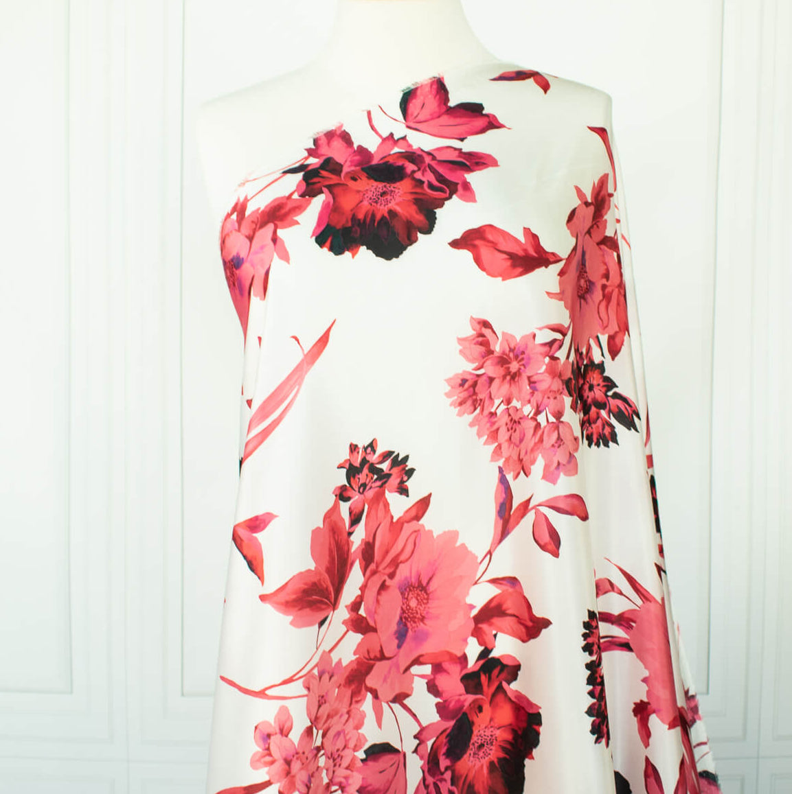 Italian Floral Silk satin designer deadstock fabric by the yard. Ready to create something gorgeous with our silk satin fabric of red and pink blooms highlighted by a bit of black for drama set against a white background. This thin woven silk from the Italian mills has a smooth satiny hand and just the right amount of flow! Image of fabric draped on dressform.