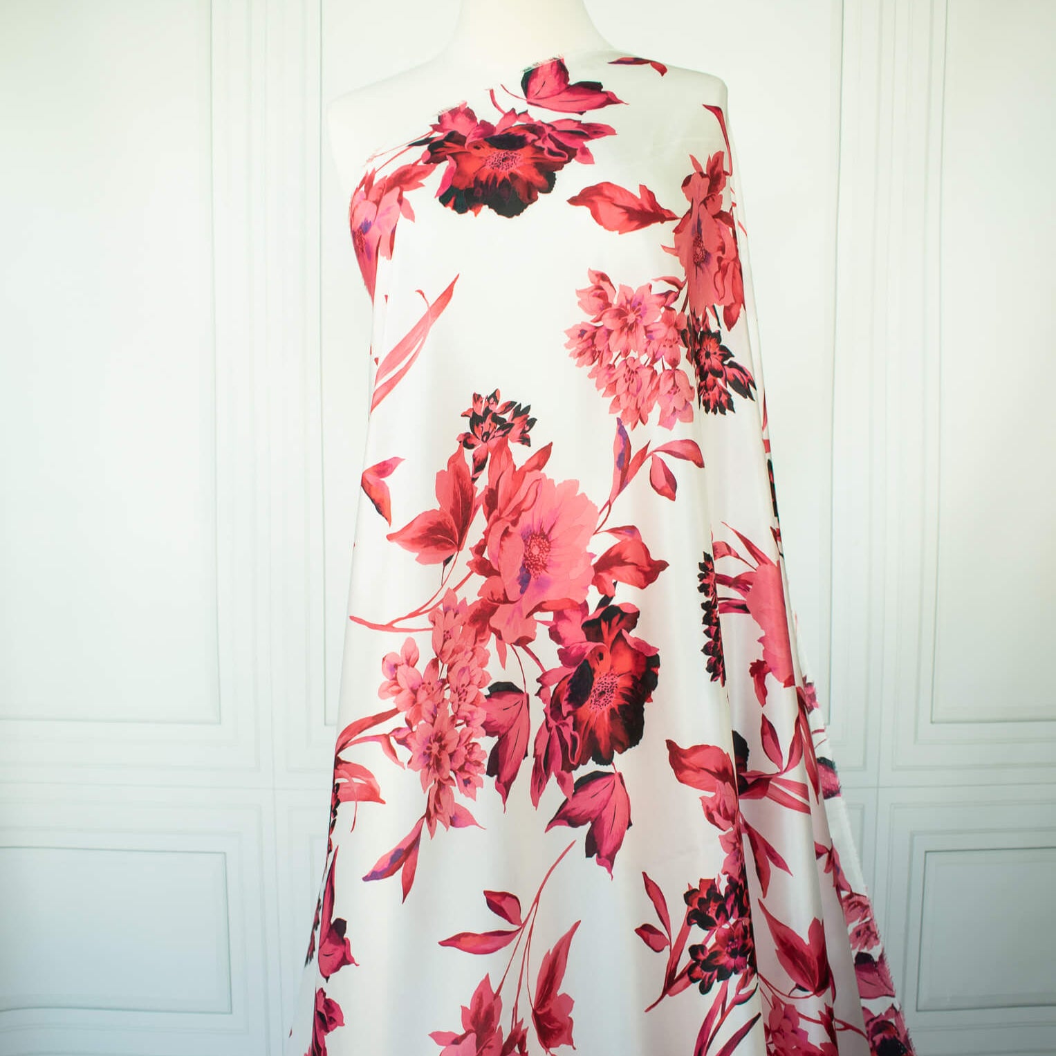 Italian Floral Silk satin designer deadstock fabric by the yard. Ready to create something gorgeous with our silk satin fabric of red and pink blooms highlighted by a bit of black for drama set against a white background. This thin woven silk from the Italian mills has a smooth satiny hand and just the right amount of flow! Image of fabric draped on dressform.