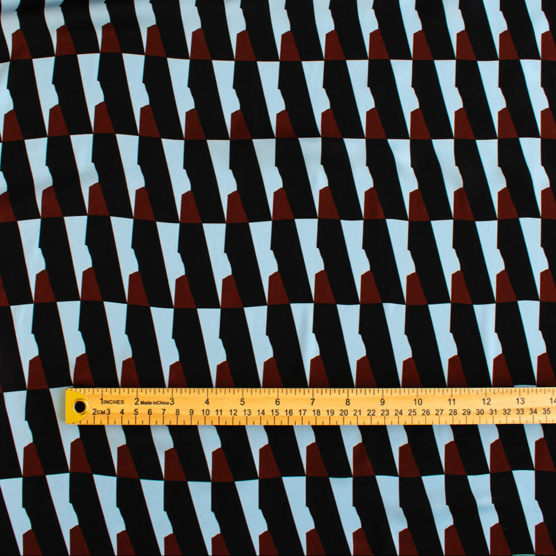 Italian Geometric Poly Satin designer deadstock fabric by the yard. From the Italian mills, a gorgeous satin with a modern palette of light blue, earthy brown and black that will elevate your next sewing project! Image of fabric scale.