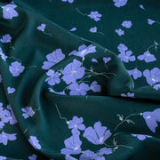 Close up of fabric design. Italian Floral Viscose Crepe designer deadstock fabric by the yard. Flowers of French Blue wisp across a deep green background that evokes a breezy mood of pleasant days.
