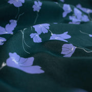 Close up image of fabric. Italian Floral Viscose Crepe designer deadstock fabric by the yard. Flowers of French Blue wisp across a deep green background that evokes a breezy mood of pleasant days.