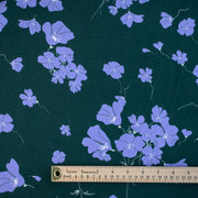 Image of fabric design with ruler. Italian Floral Viscose Crepe designer deadstock fabric by the yard. Flowers of French Blue wisp across a deep green background that evokes a breezy mood of pleasant days.