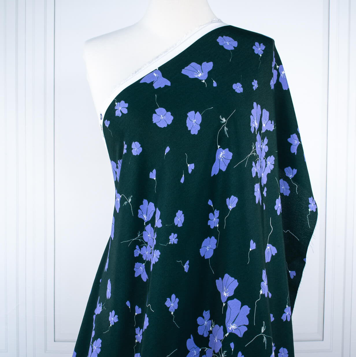 Image of draped on dressform. Italian Floral Viscose Crepe designer deadstock fabric by the yard. Flowers of French Blue wisp across a deep green background that evokes a breezy mood of pleasant days.