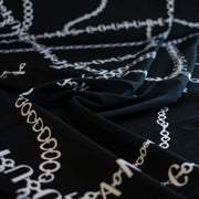 Italian High-End Designer Couture Knit in Black designer deadstock fabric by the yard. Classic \/ers@ce ITY jersey knit featuring white chains with the designer name and 'Couture' wording against a black background.
Close up image.