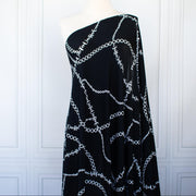 Italian High-End Designer Couture Knit in Black designer deadstock fabric by the yard. Classic \/ers@ce ITY jersey knit featuring white chains with the designer name and 'Couture' wording against a black background.  Image of fabric on dressform.