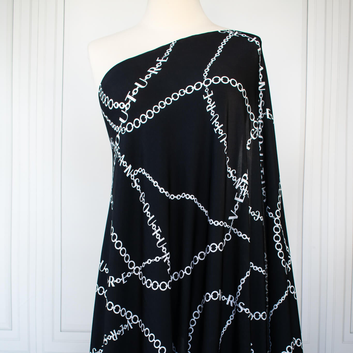 Italian High-End Designer Couture Knit in Black designer deadstock fabric by the yard. Classic \/ers@ce ITY jersey knit featuring white chains with the designer name and 'Couture' wording against a black background.  Image of fabric on dressform.