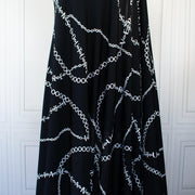 Italian High-End Designer Couture Knit in Black designer deadstock fabric by the yard. Classic \/ers@ce ITY jersey knit featuring white chains with the designer name and 'Couture' wording against a black background.  Image of fabric drape.