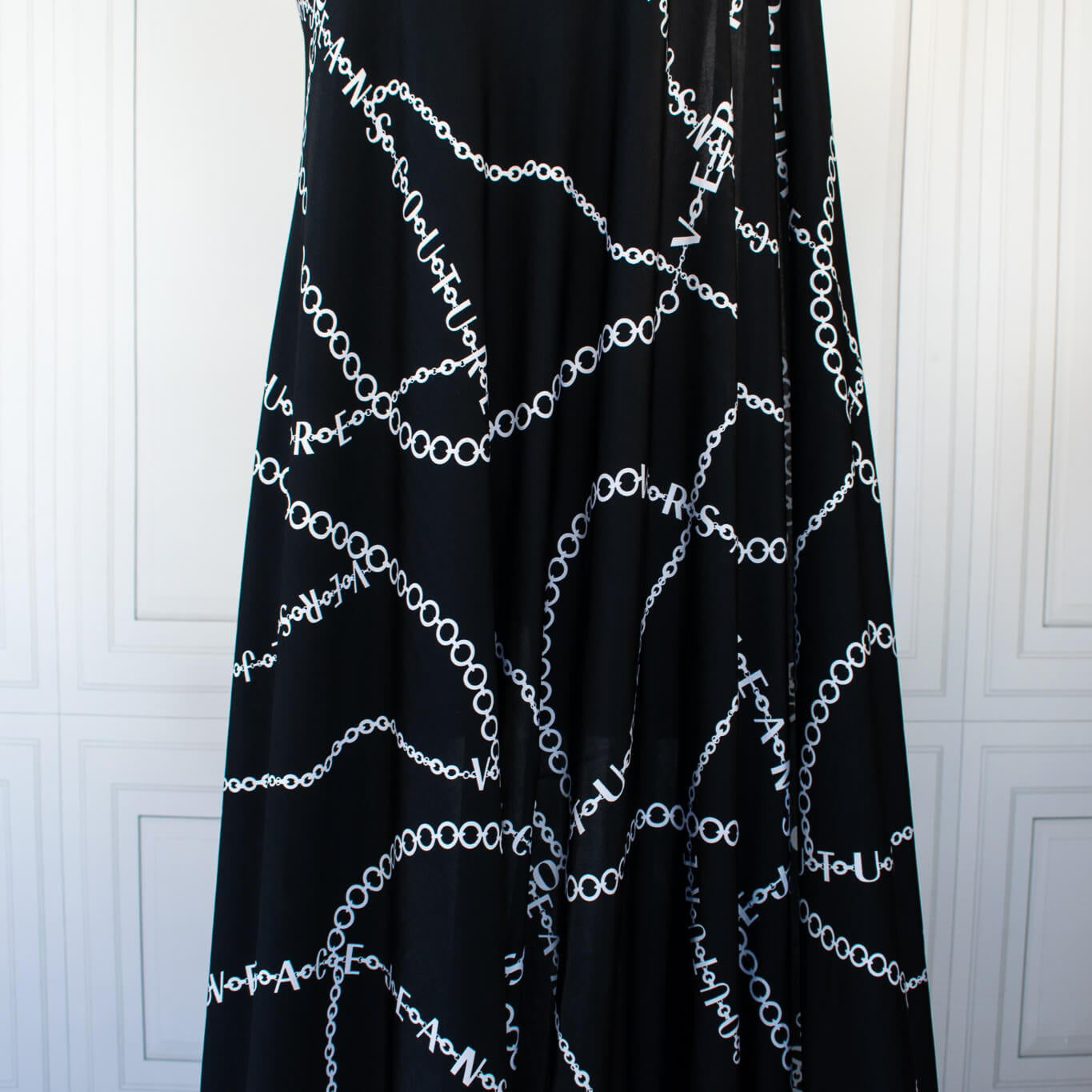 Italian High-End Designer Couture Knit in Black designer deadstock fabric by the yard. Classic \/ers@ce ITY jersey knit featuring white chains with the designer name and 'Couture' wording against a black background.  Image of fabric drape.