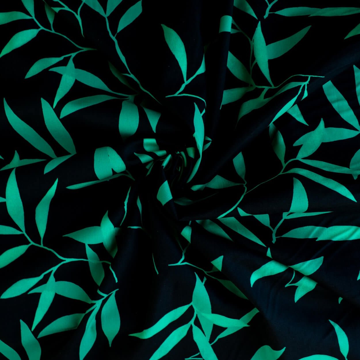 Carolina' cotton poplin designer fabric by the yard. This Italian poplin is light and billowy, perfect for sewing up tops, dresses and skirts. Made with stretch for ultimate comfort, this fabric is perfect if you want to add a touch of the exotic with its turquoise bamboo leaf print set against a black background. Image of fabric fullness.