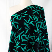 Carolina' cotton poplin designer fabric by the yard. This Italian poplin is light and billowy, perfect for sewing up tops, dresses and skirts. Made with stretch for ultimate comfort, this fabric is perfect if you want to add a touch of the exotic with its turquoise bamboo leaf print set against a black background. Image of fabric draped on dressform.