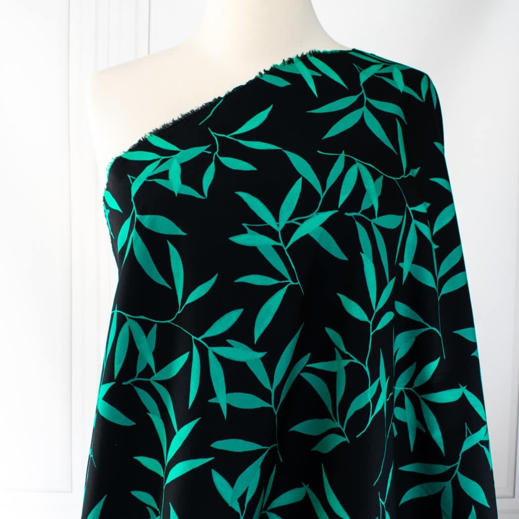 Carolina' cotton poplin designer fabric by the yard. This Italian poplin is light and billowy, perfect for sewing up tops, dresses and skirts. Made with stretch for ultimate comfort, this fabric is perfect if you want to add a touch of the exotic with its turquoise bamboo leaf print set against a black background. Image of fabric draped on dressform.