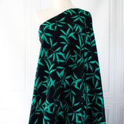 Carolina' cotton poplin designer fabric by the yard. This Italian poplin is light and billowy, perfect for sewing up tops, dresses and skirts. Made with stretch for ultimate comfort, this fabric is perfect if you want to add a touch of the exotic with its turquoise bamboo leaf print set against a black background. Image of fabric draped on dressform full length.