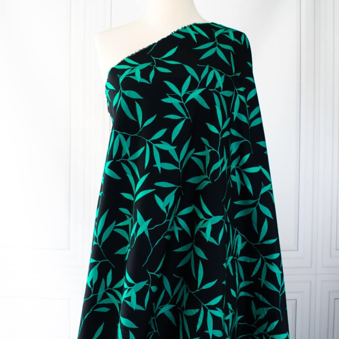 Carolina' cotton poplin designer fabric by the yard. This Italian poplin is light and billowy, perfect for sewing up tops, dresses and skirts. Made with stretch for ultimate comfort, this fabric is perfect if you want to add a touch of the exotic with its turquoise bamboo leaf print set against a black background. Image of fabric draped on dressform full length.