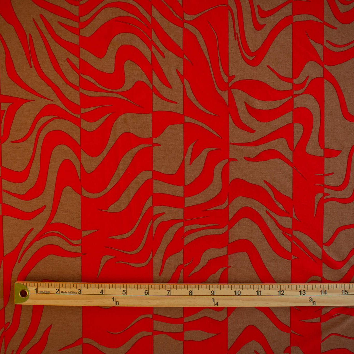 Italian Single Viscose Jersey Red and Caramel Modern Print fabric by the yard. A gorgeous vibrant knit that is sure to capture compliments. We love this combination of red and caramel brown tones in this modern jersey knit fabric. The printed design has a bit of animal print edge in a stripe like pattern.  Image of fabric design scale with ruler.