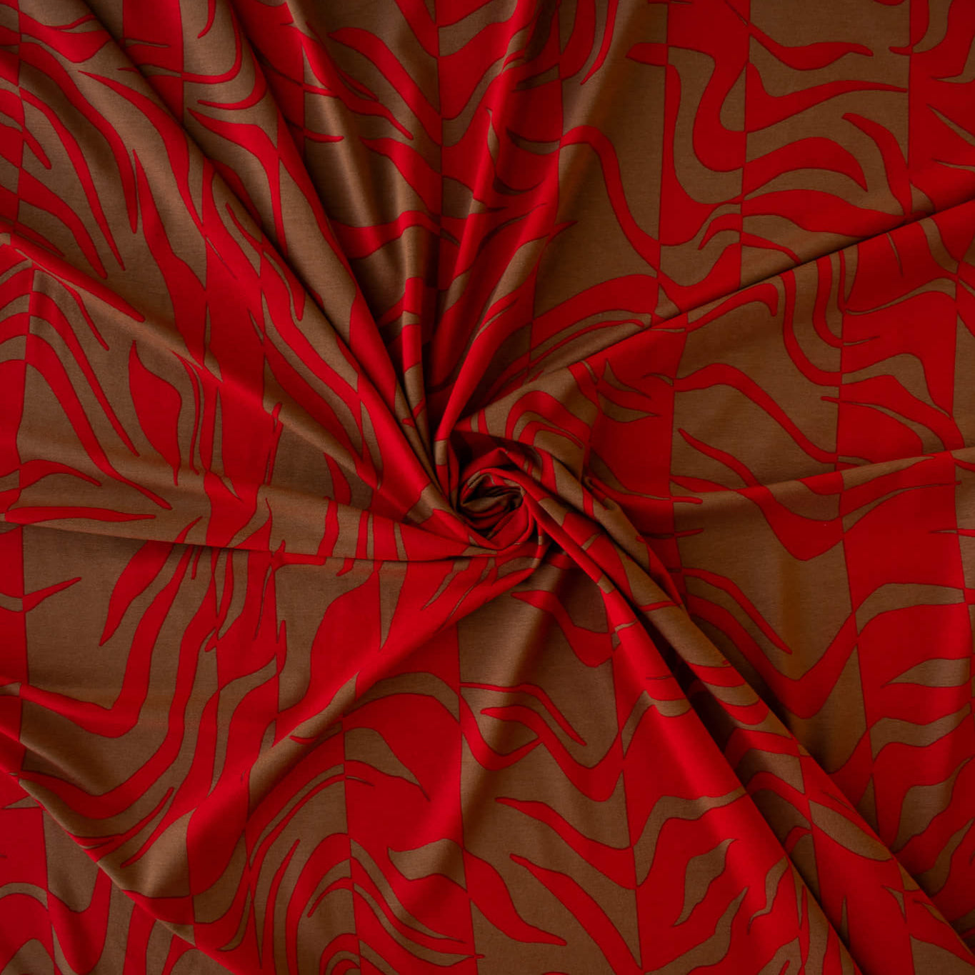 Italian Single Viscose Jersey Red and Caramel Modern Print fabric by the yard. A gorgeous vibrant knit that is sure to capture compliments. We love this combination of red and caramel brown tones in this modern jersey knit fabric. The printed design has a bit of animal print edge in a stripe like pattern.  Image of fabric fullness.