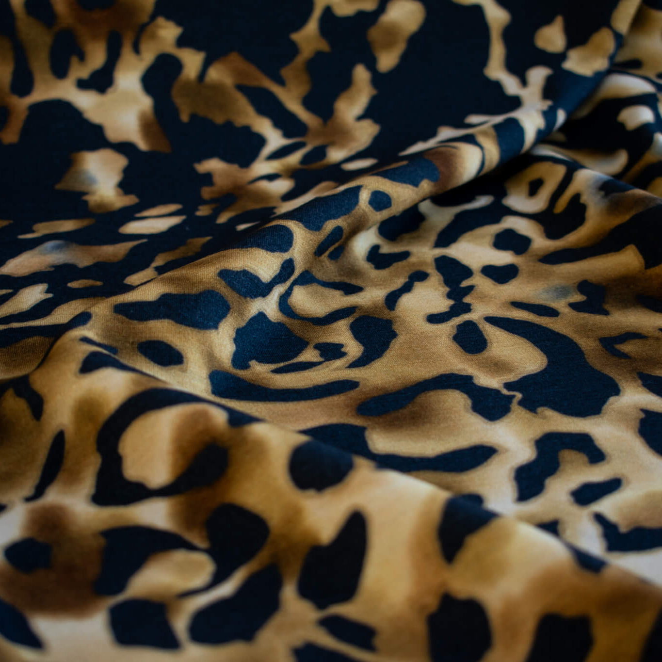 Italian Animal Print Wool Blend Jersey knit fabric by the yard. Shades of gold and cream flow against dramatic coal a bits of blue to create a vibrant and sophisticated animal print design. This would make a lovely wrap style long cardigan, a bold fitted sheath dress, or pencil skirt. Close up image.