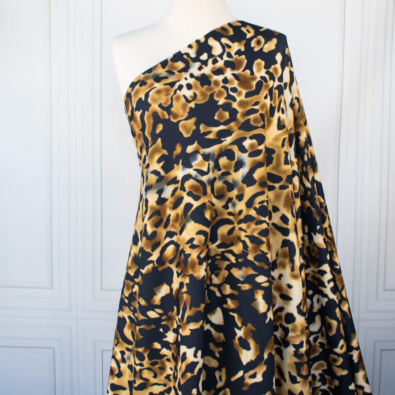 Italian Animal Print Wool Blend Jersey knit fabric by the yard. Shades of gold and cream flow against dramatic coal a bits of blue to create a vibrant and sophisticated animal print design. This would make a lovely wrap style long cardigan, a bold fitted sheath dress, or pencil skirt. Image of fabric draped on dressform.