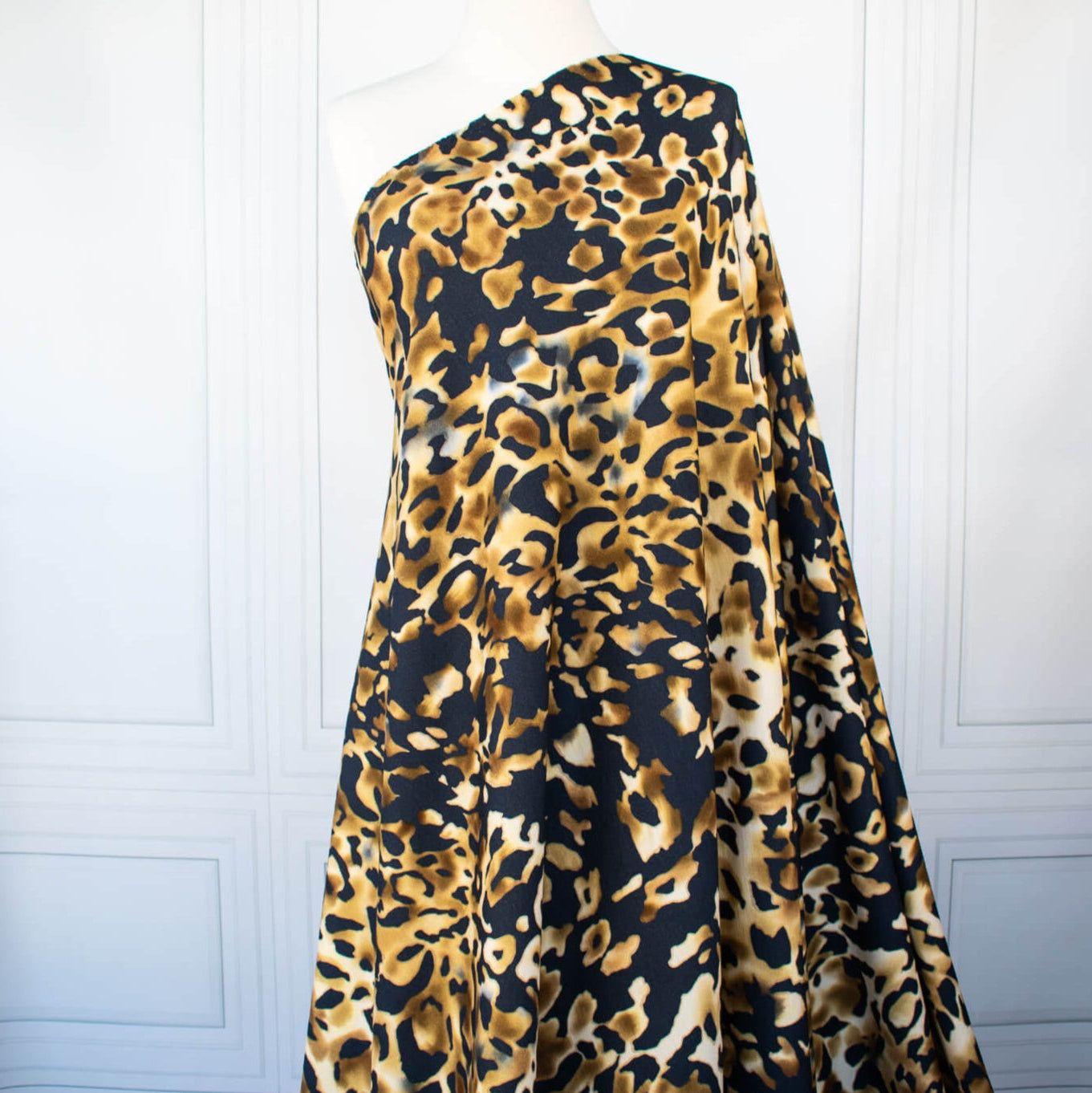 Italian Animal Print Wool Blend Jersey knit fabric by the yard. Shades of gold and cream flow against dramatic coal a bits of blue to create a vibrant and sophisticated animal print design. This would make a lovely wrap style long cardigan, a bold fitted sheath dress, or pencil skirt. Image of fabric draped on dressform.