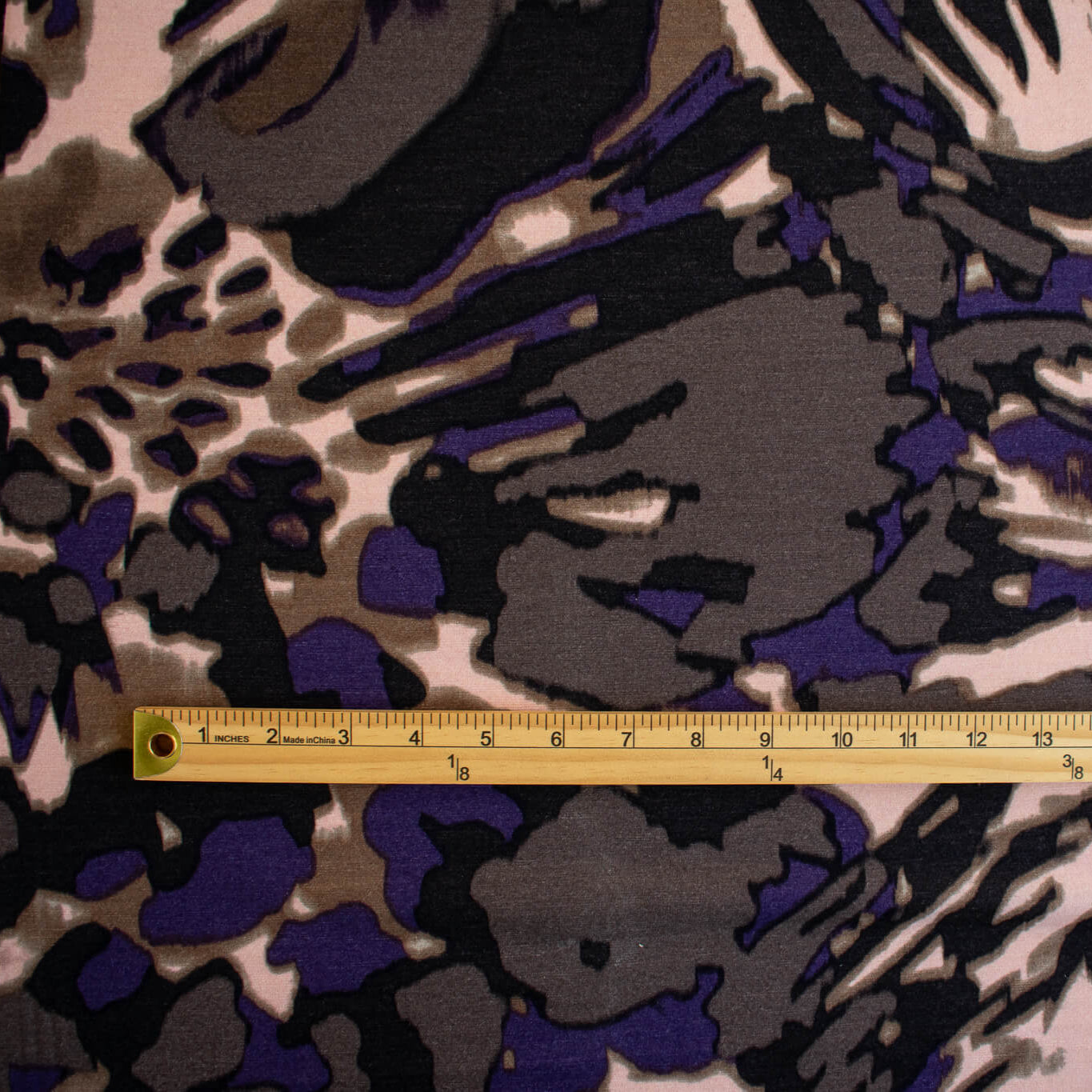 Italian Modern Floral Single Jersey Wool blend fabric by the yard. Gorgeous modern floral print perfect for transitioning to warmer months. This wool blend jersey in shades of brown, light pink, purple and black has a soft hand a beautiful drape. Whether you are creating a T-shirt or something a bit fancier, you're going to love how this fabric feels against your skin. Image of fabric design scale with ruler.