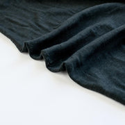 NYC High-End Designer Black Cotton Jersey Knit fabric by the yard. This deadstock fabric is the perfect sustainable choice for creating soft, flowy pieces that are both stylish and playful. It has a soft hand and translucent quality, and the extra wide width allows for versatile designs. Image of selvedge.