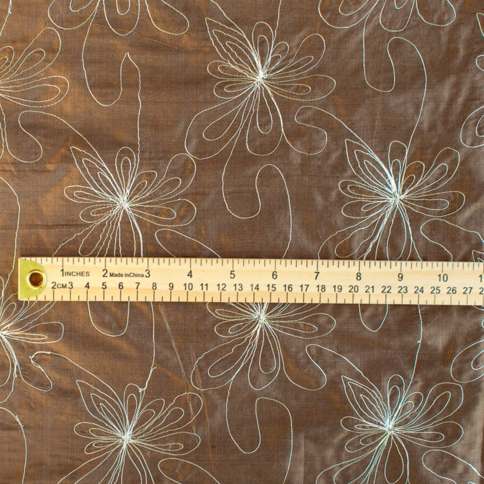 100% silk shantung fabric by the yard featuring a metallic embroidered floral design in a modern and playful hand-drawn style. In a rich hazelnut brown hue, this fabric offers a crisp and light textured hand, with a soft sheen for added elegance. Image of pattern scale.