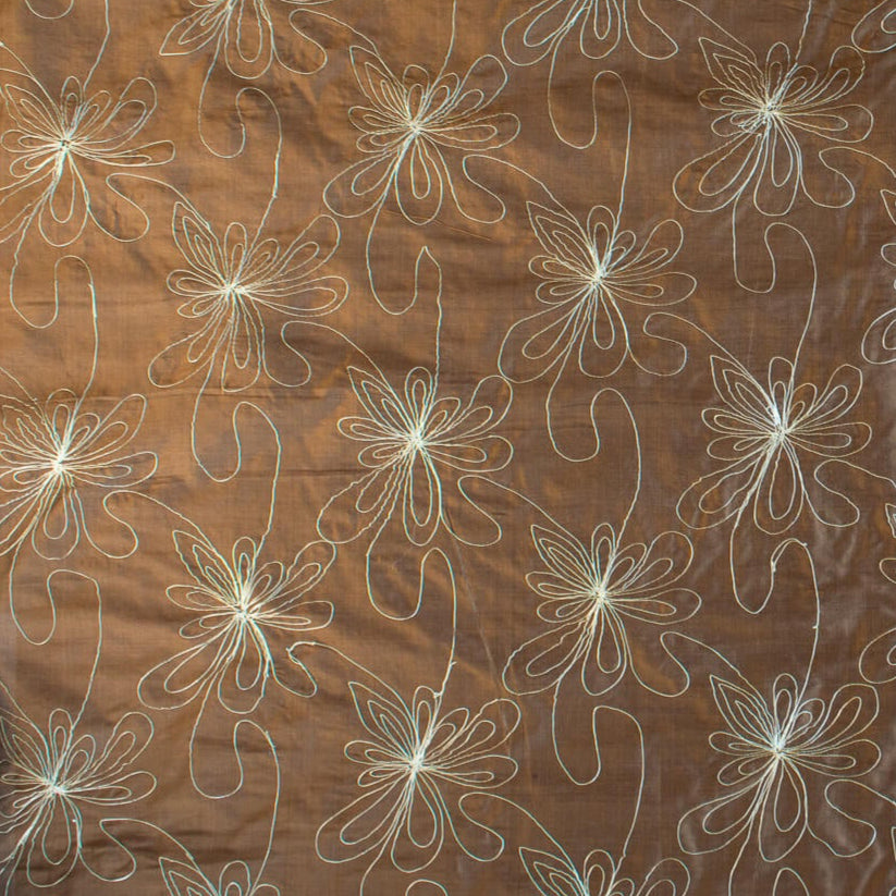 100% silk shantung fabric by the yard featuring a metallic embroidered floral design in a modern and playful hand-drawn style. In a rich hazelnut brown hue, this fabric offers a crisp and light textured hand, with a soft sheen for added elegance. Image of fabric design.
