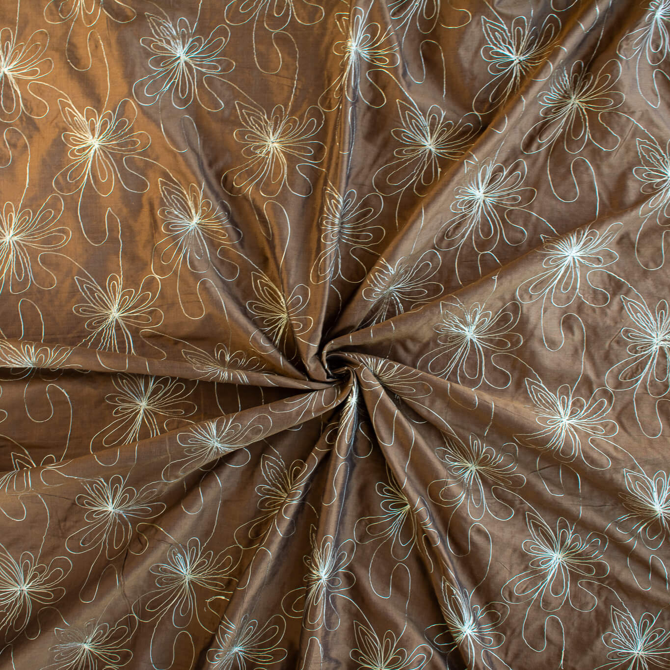 100% silk shantung fabric by the yard featuring a metallic embroidered floral design in a modern and playful hand-drawn style. In a rich hazelnut brown hue, this fabric offers a crisp and light textured hand, with a soft sheen for added elegance. Image of fabric fullness.