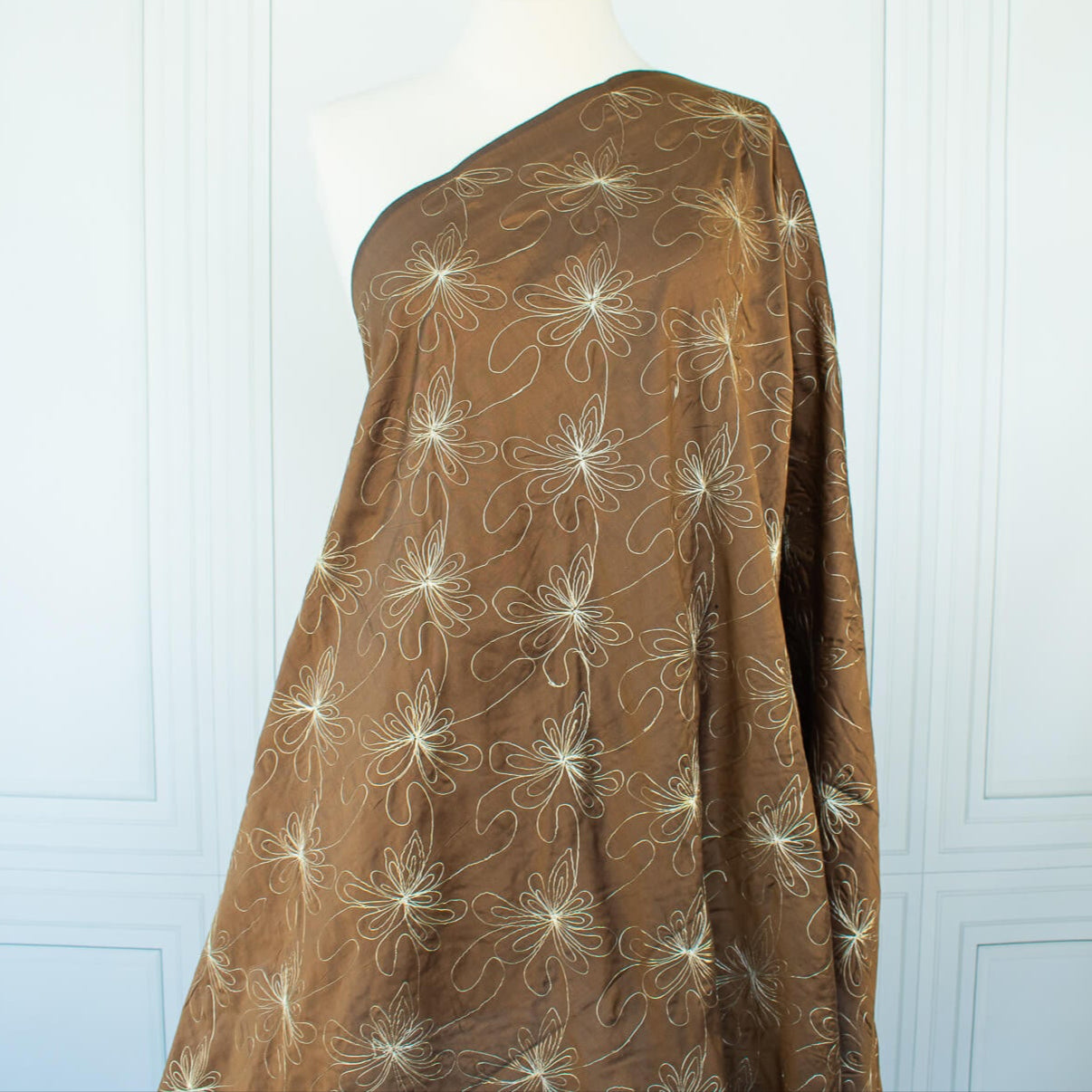 100% silk shantung fabric by the yard featuring a metallic embroidered floral design in a modern and playful hand-drawn style. In a rich hazelnut brown hue, this fabric offers a crisp and light textured hand, with a soft sheen for added elegance. Image of fabric on dressform.