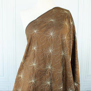 100% silk shantung fabric by the yard featuring a metallic embroidered floral design in a modern and playful hand-drawn style. In a rich hazelnut brown hue, this fabric offers a crisp and light textured hand, with a soft sheen for added elegance. Image of fabric on dressform.