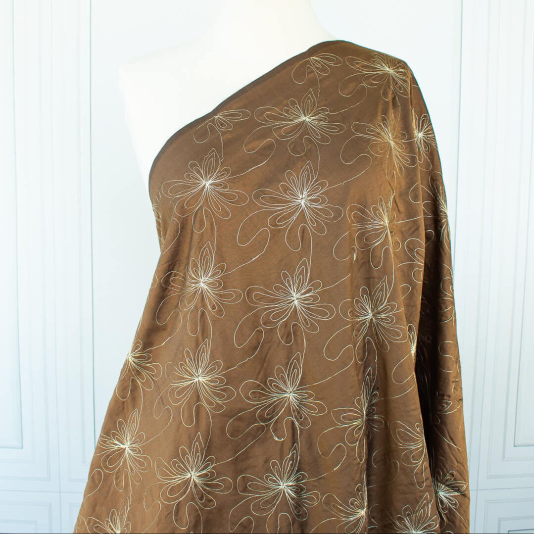 100% silk shantung fabric by the yard featuring a metallic embroidered floral design in a modern and playful hand-drawn style. In a rich hazelnut brown hue, this fabric offers a crisp and light textured hand, with a soft sheen for added elegance. Image of fabric on dressform.
