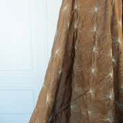 100% silk shantung fabric by the yard featuring a metallic embroidered floral design in a modern and playful hand-drawn style. In a rich hazelnut brown hue, this fabric offers a crisp and light textured hand, with a soft sheen for added elegance. Image of fabric drape.