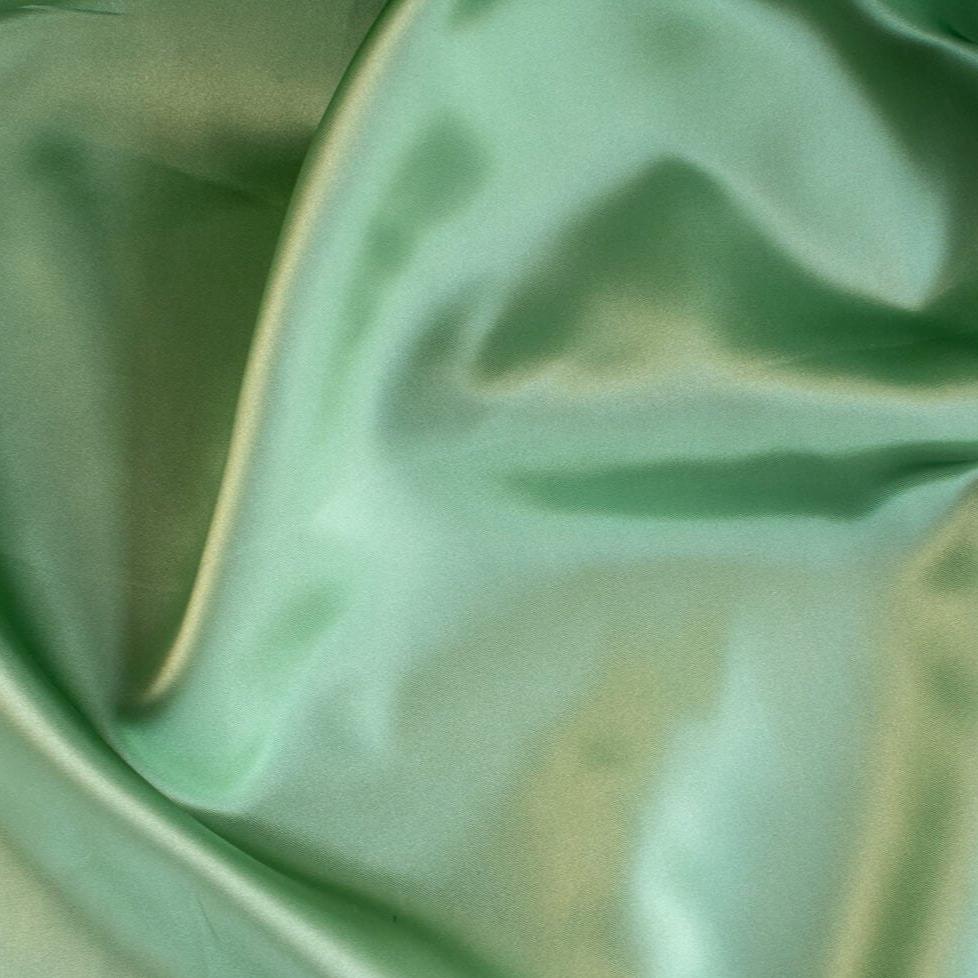 NYC Designer Polyester Satin designer deadstock fabric by the yard. Shimmery satin in a serene spring green is sophisticated and eye catching!  This opaque, tightly woven fabric falls moderately away from the body. Close up image.
