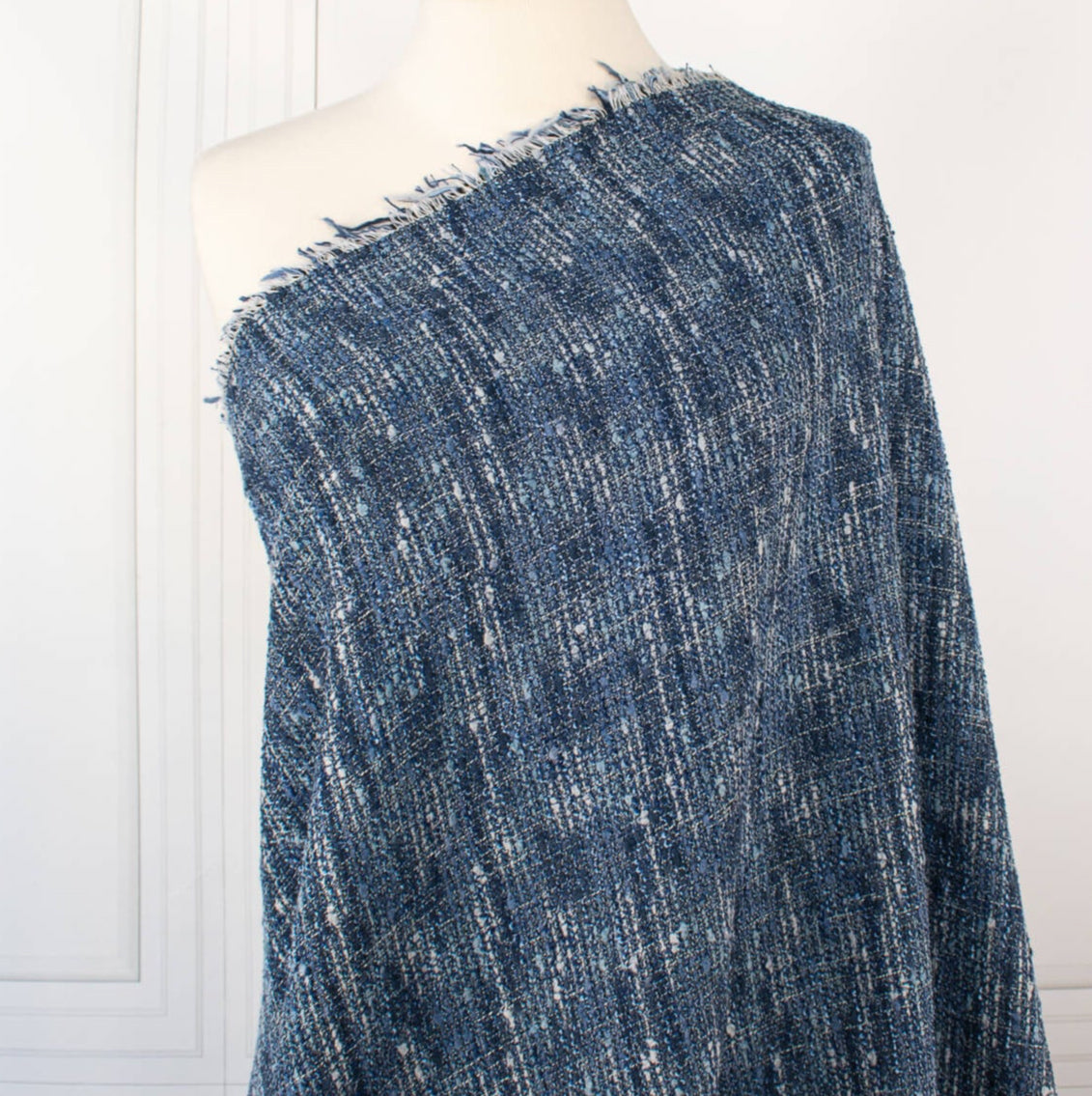 A beautifully soft NYC Designer Boucle suiting fabric by the yard that can be paired with sophisticated solids or your favorite denim. Varying shades of blue and alabaster yarns make this boucle extra special. Enjoy creating your next make with style and comfort. Image of fabric draped on dressform.