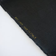 Italian, rich black 100% Linen fabric by the yard in a lovely mid-weight. The soft, crisp, and semi-textured hand of this fabric is perfect for creating sophisticated vests, dresses, suits, and skirts. This breathable fabric is perfect for warmer weather, making it a must-have for any fashion enthusiast. Image of fabric selvedge.