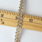 This stunning vintage gimp trim is the perfect addition to any couture garment. Our narrow trim is crafted from a mix of silver and champagne gold metallic threads, making it a designer's dream. A timeless piece, this trim is sure to elevate any project with its timeless charm. Pictured with ruler for width.