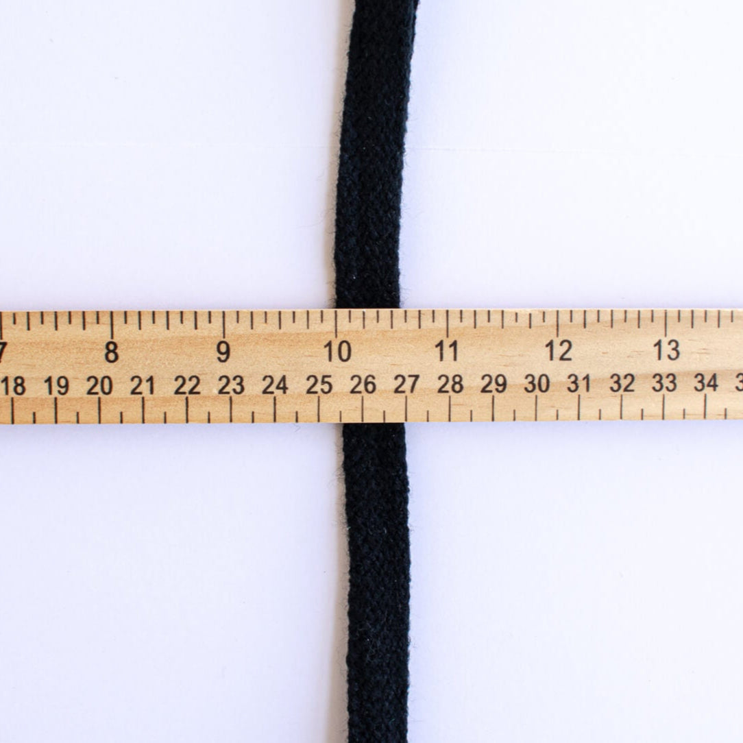 Vintage Foldover Black Braid Trim is back! This soft 1 inch trim can be folded to a sleek half-inch, perfect for a clean final touch on garment edges. Image of trim folded with ruler demonstrating trim width.