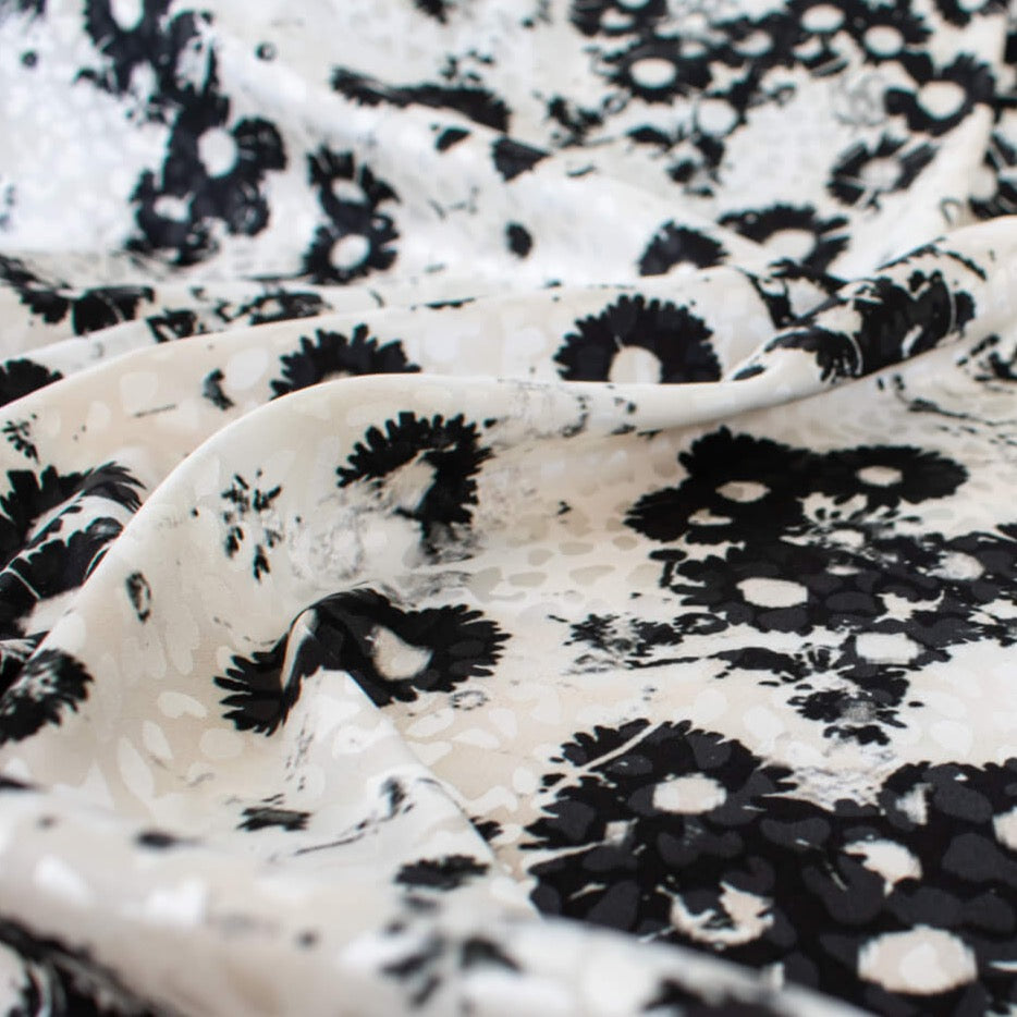 Close up image of couture black and creamy white floral Jacquard. This designer deadstock fabric features a stunning modern black daisy design set against a white shimmery jacquard.