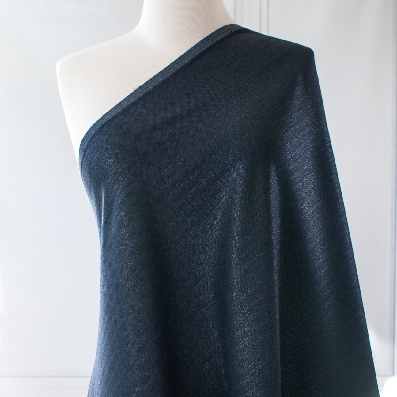 Image of fabric draped on dressform. A gorgeous wool blend suiting from a Beverly Hills couture house is sure to add glamour to your outfit!  A soft textured hand with a herringbone stripe pattern that shimmers with silvery metallic threads. A perfect choice for ;a jacket, skirt, wide leg pant, or perhaps a coat dress.