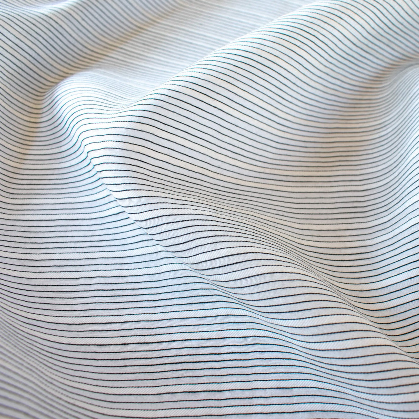 Light and airy Italian voile is soft and ohh so summery! Can you just picture yourself in a loose fitted unbuttoned shirtdress as a gorgeous layering piece over a cami and ankle length jeans. This will definitely take your summer holiday up a notch! Perfect for summer dresses, skirts and tops. The thin horizontal black stripes and bright white woven opaque stripes are set against a sheer white voile Close up image.