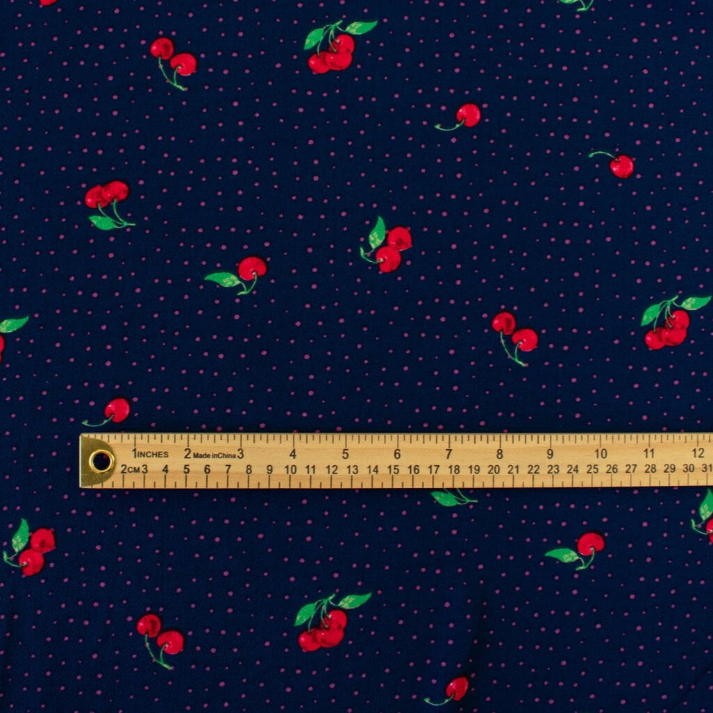 Have some fun with our navy and pink polka dot designer deadstock fabric by the yard adorned with vibrant red cherries. Made from high-quality polyester crepe, this fabric has a textured hand, lovely drape, and a vintage vibe. Image of pattern scale with ruler.