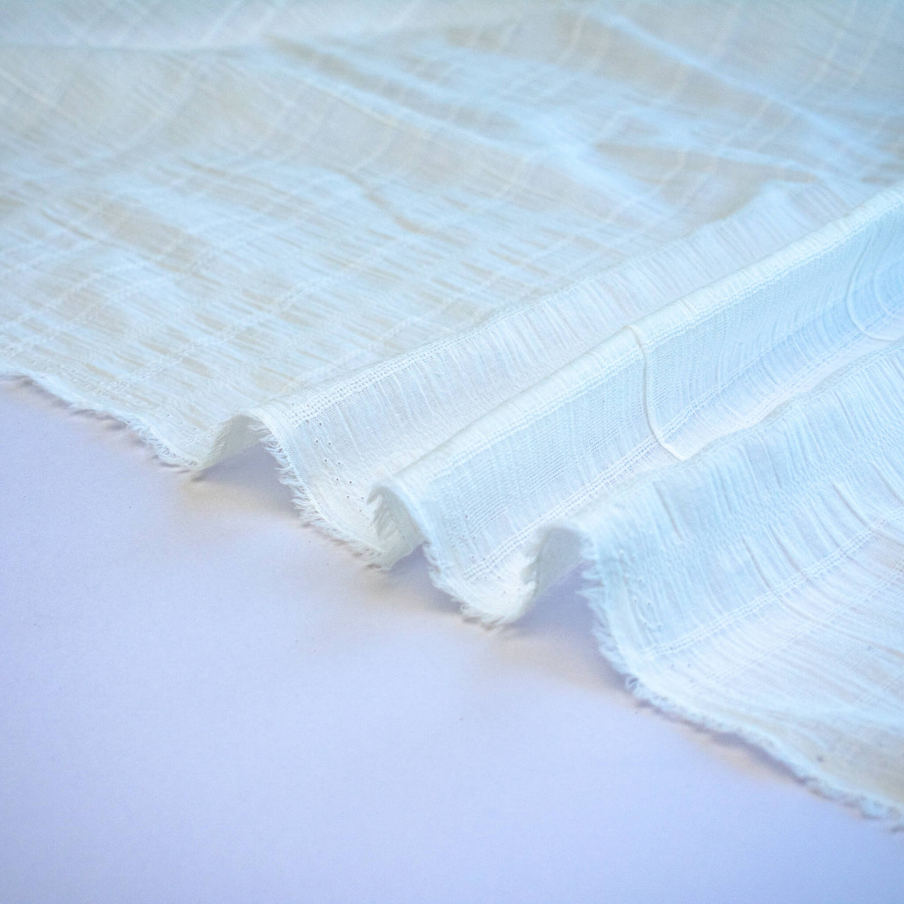 Close-up of a textured white fabric selvedge on a light background