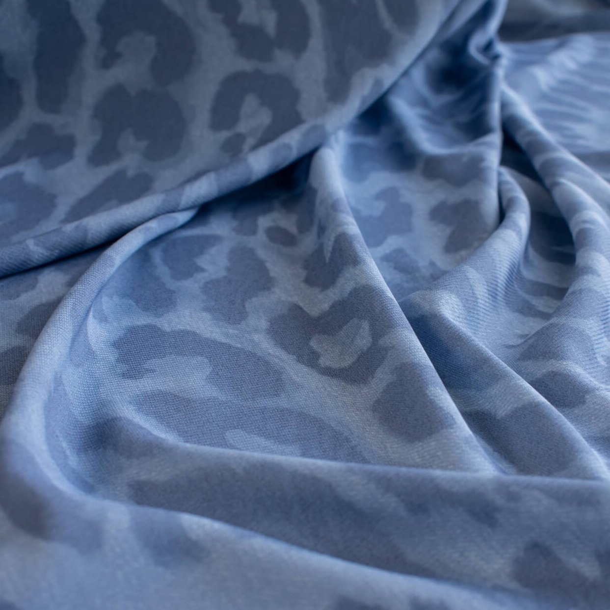 French Animal Print Fine Knit Crepe fabric by the yard in shades of blue. Liven up your next project with a gorgeous animal print that pairs well with navy, gray, purple and white. This translucent fine crepe has a lightly textured hand, a bit of stretch, and a lovely graceful drape. Close up image of fabric.