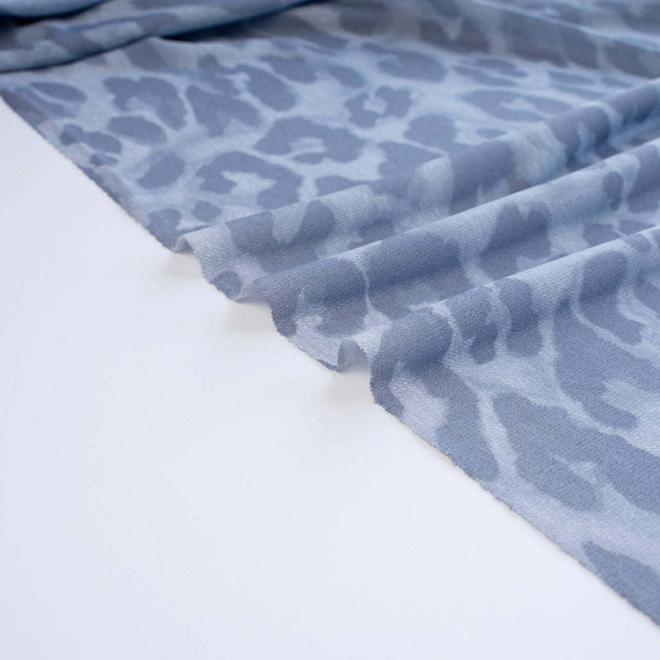 French Animal Print Fine Knit Crepe fabric by the yard in shades of blue. Liven up your next project with a gorgeous animal print that pairs well with navy, gray, purple and white. This translucent fine crepe has a lightly textured hand, a bit of stretch, and a lovely graceful drape. Image of selvedge.