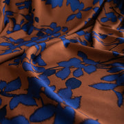 Close up image of Italian Viscose Ikat Floral Challis designer deadstock fabric by the yard. Ikat leaves of deep indigo set against a rich burnt Sienna background in this digitally printed challis is simply gorgeous. 