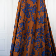 Image of fabric drape. Italian Viscose Ikat Floral Challis designer deadstock fabric by the yard. Ikat leaves of deep indigo set against a rich burnt Sienna background in this digitally printed challis is simply gorgeous. 