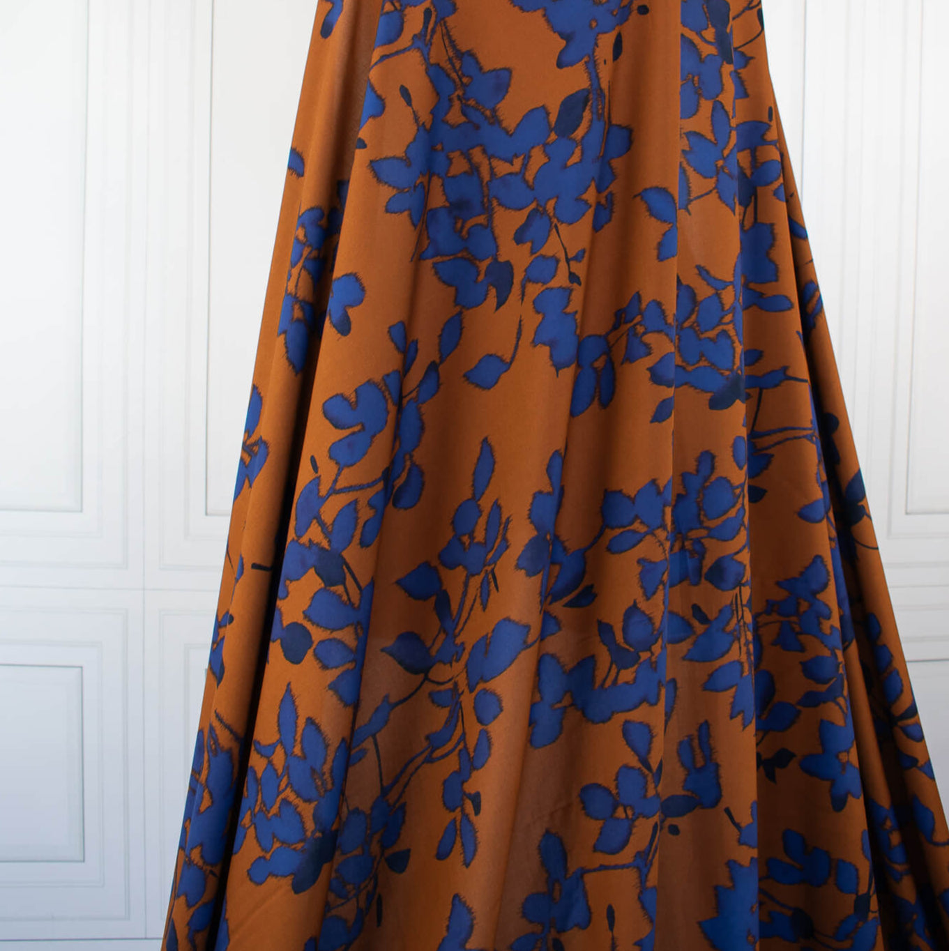 Image of fabric drape. Italian Viscose Ikat Floral Challis designer deadstock fabric by the yard. Ikat leaves of deep indigo set against a rich burnt Sienna background in this digitally printed challis is simply gorgeous. 