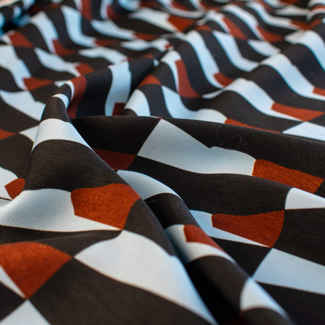 Italian Geometric Poly Satin designer deadstock fabric by the yard. From the Italian mills, a gorgeous satin with a modern palette of light blue, earthy brown and black that will elevate your next sewing project! Close up image.