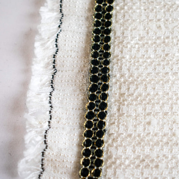Create a luxurious touch of couture with our vintage trim as it’s metallic gold threading elegantly encircles soft black ribbons. It is sure to make any fabric you are working with sophisticated and glamourous. Photo of trim displayed atop boucle fabric. Fabric sold separately.